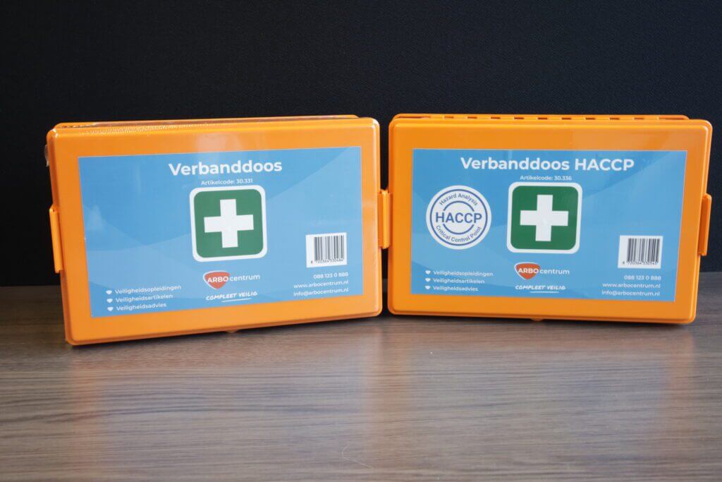 Twee oranje EHBO-koffers met het label Verbanddoos en Verbanddoos HACCP, elk met een groen kruis, rusten naast elkaar op een houten oppervlak tegen een donkere achtergrond. Met contactgegevens en een logo onderstrepen ze 5 redenen om een verbanddoos te hebben.
