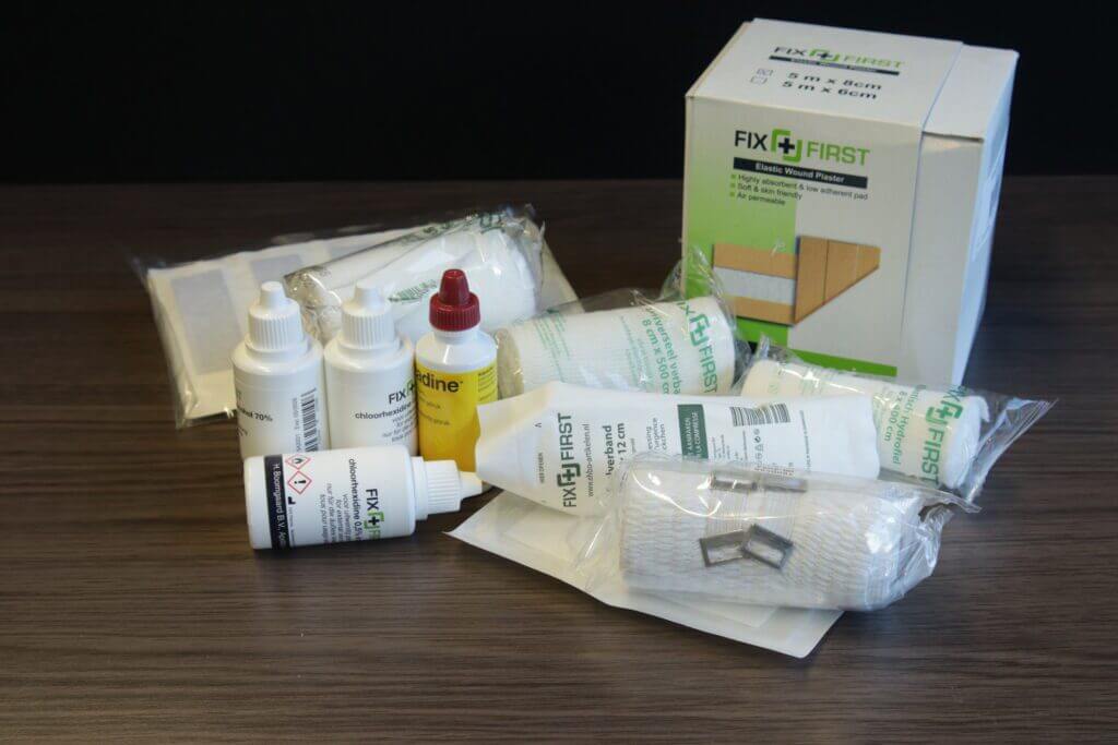Een verzameling eerstehulpmaterialen staat op een tafel, met verbanden, flessen met antiseptische oplossingen en gaasverbanden. De FIX FIRST-merkdoos bevat essentiƫle benodigdheden en tips voor het goed verzorgen van een open wond, zodat u voorbereid bent op kleine noodgevallen.