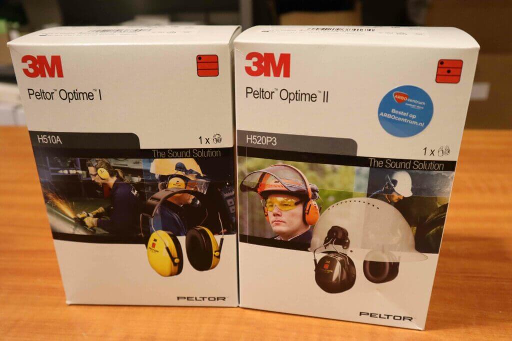 Op een houten oppervlak roepen twee dozen met 3M Peltor Optime gehoorbescherming de vraag op: Wanneer draag je wel of geen gehoorbescherming? De linkerdoos, met het label H510A, toont oorkappen in gebruik, terwijl de rechterdoos, met het label H520P3, oorkappen toont die op een helm zijn bevestigd.