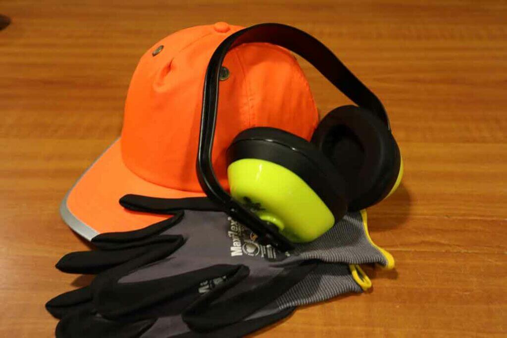 Om deze belangrijkste redenen haal jij je VCA-diploma: een oranje veiligheidsmuts, gele oorbeschermers en zwartgrijze handschoenen liggen netjes gerangschikt op een houten oppervlak.