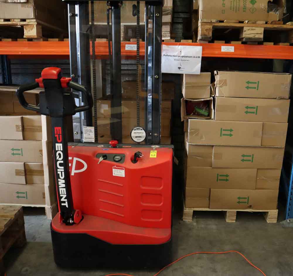 In deze situatie kies je voor het gebruik van een stapelaar, zoals de rood-zwarte elektrische palletstapelaar met het label EP EQUIPMENT, die in een magazijn staat te midden van gestapelde dozen en houten pallets, met daarboven een metalen schaap.