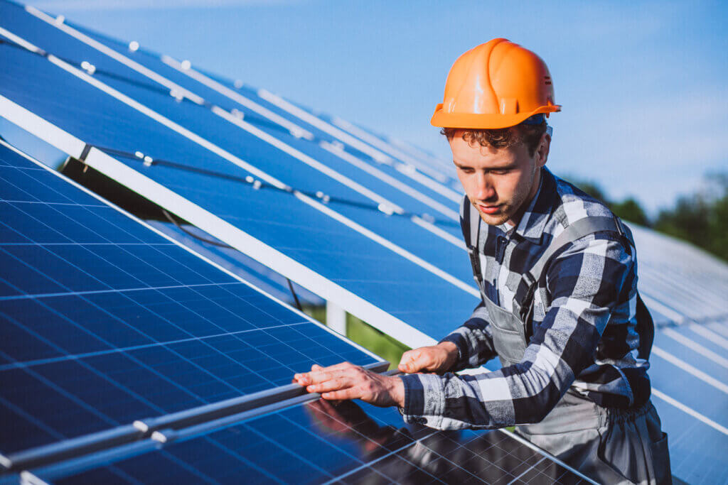 A person wearing a hard hat and a plaid shirt inspects the solar panels outdoors, embodying Valgevaars commitment to safety. They are focused on the surface of the panels, under a clear blue sky.