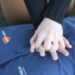 A person demonstrates CPR by performing chest compressions on anothers torso during a reanimatie cursus. The individual receiving CPR is wearing a blue shirt.